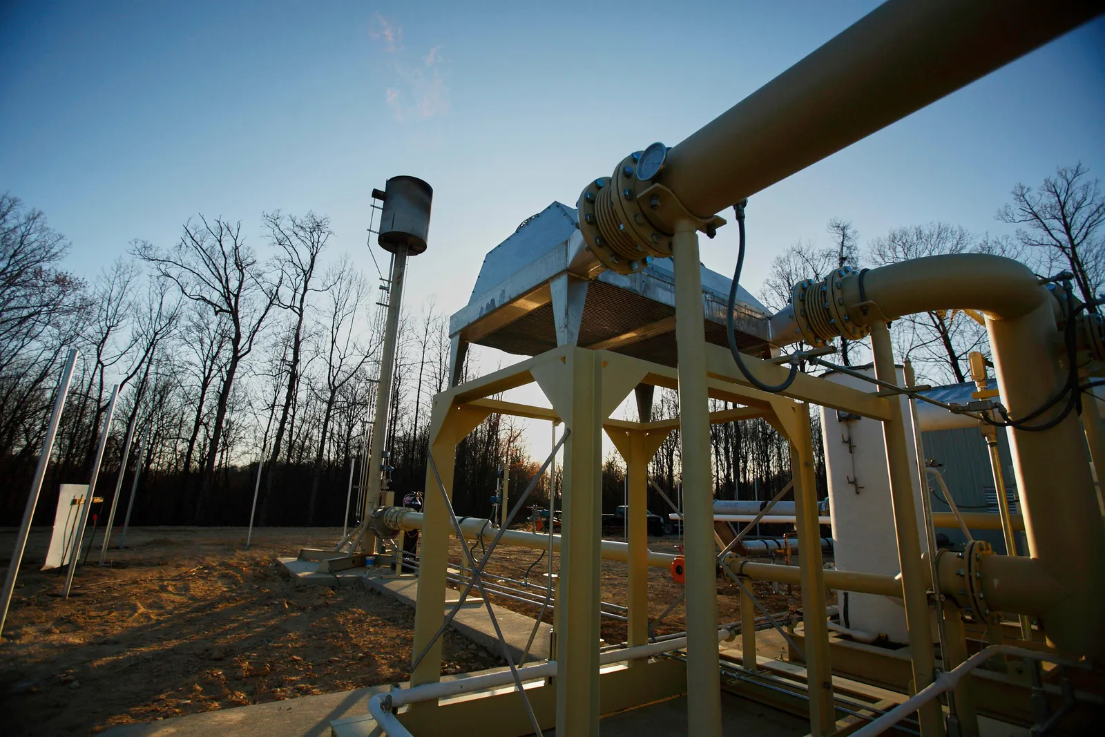 An industrial landfill site surrounded by trees is equipped with gas collection infrastructure, including vertical extraction wells and piping systems, capturing methane emissions from decomposing waste. 