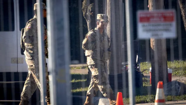 Two people dressed in fatigues walking behind a fence.