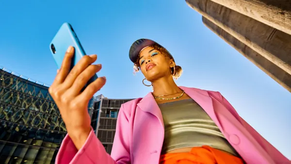 An influencer in a brightly colored outfit stares at a smartphone while standing outside