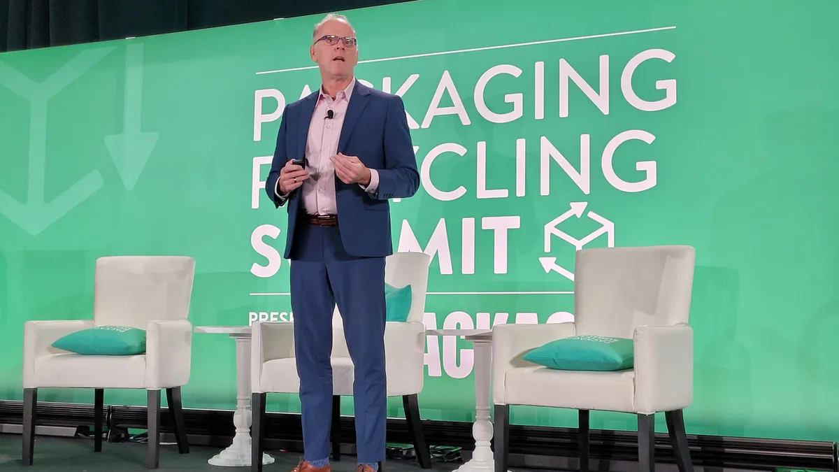 A person speaks on a stage in front of a green background that says Packaging Recycling Summit.