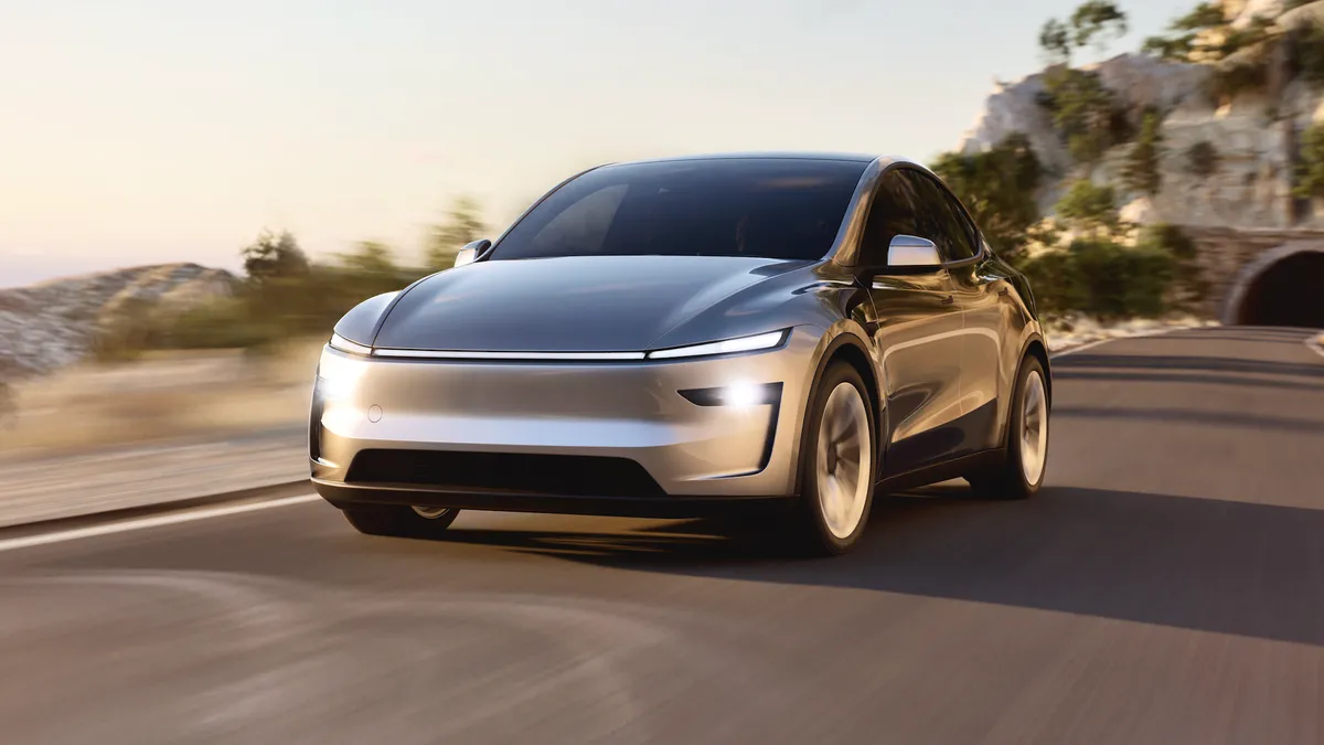 A gray Tesla Model Y driving on a road with a tunnel in the background.