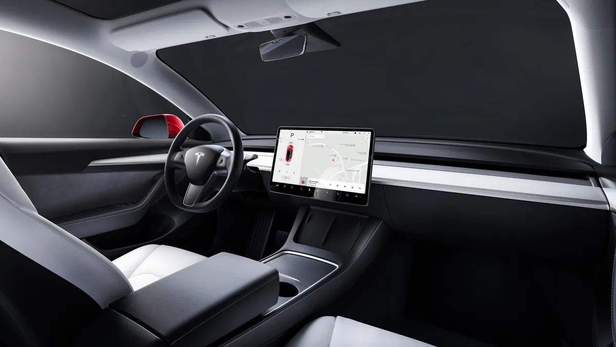 The interior view of the Tesla Model 3 showing the steering wheel and dashboard on the driver's side.