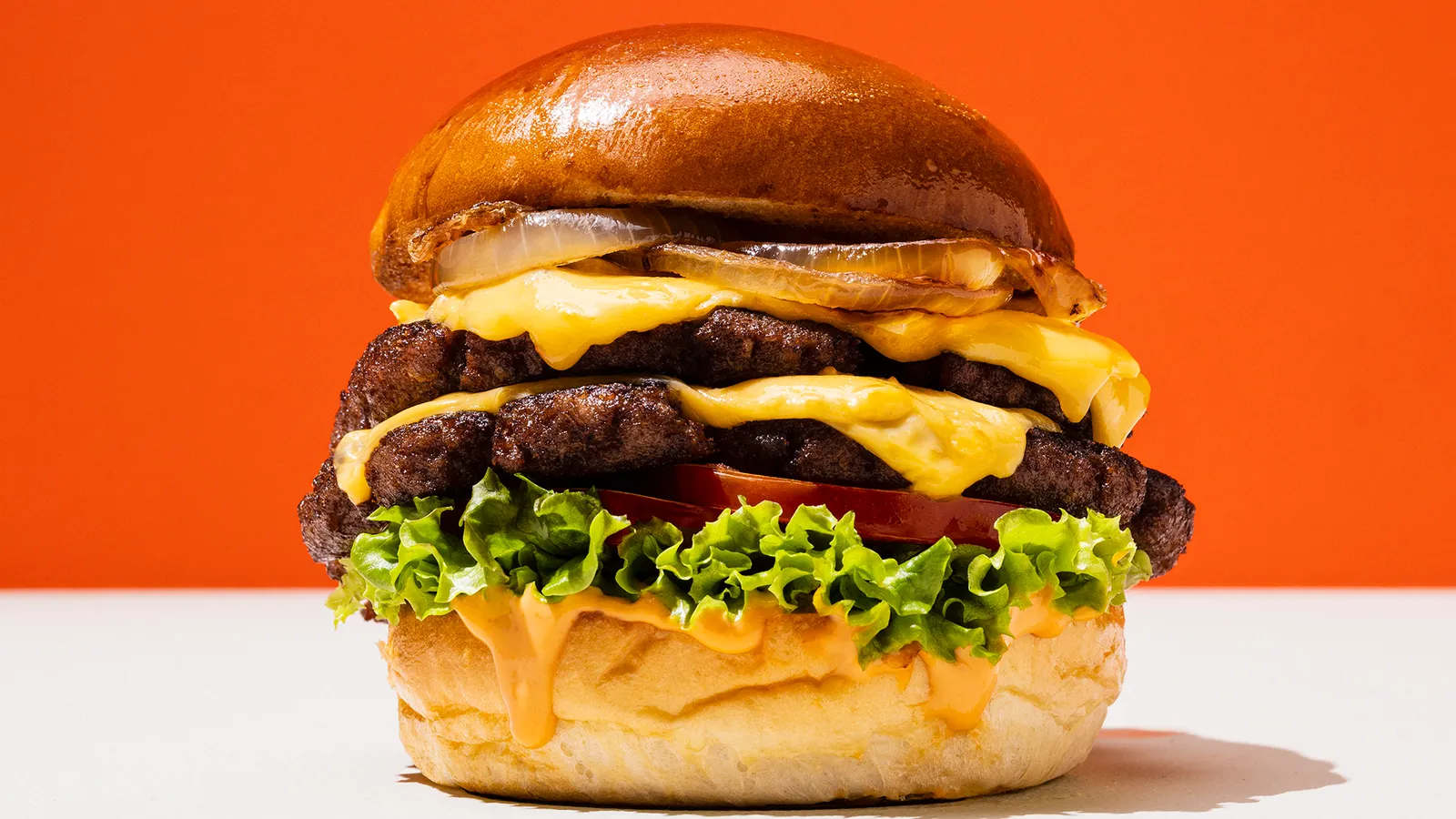 A burger made from Omeat's cultivated beef cooks on a grill. A spatula is underneath it, poised to flip it over.