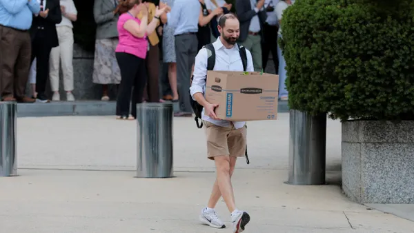 A person walks away from a building carrying items in a cardboard box.