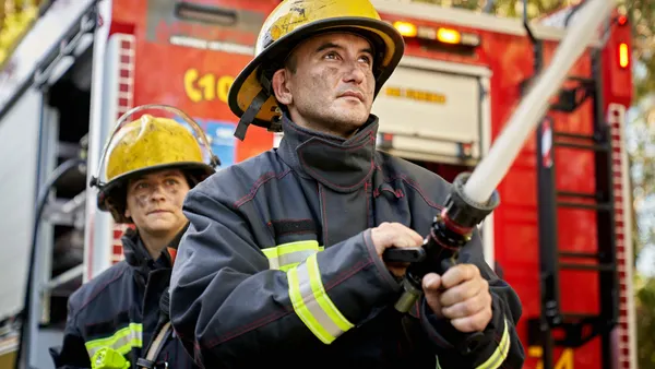 Low angle view of Caucasian first responders in their 30s holding and supporting nozzle as it shoots straight stream of water.