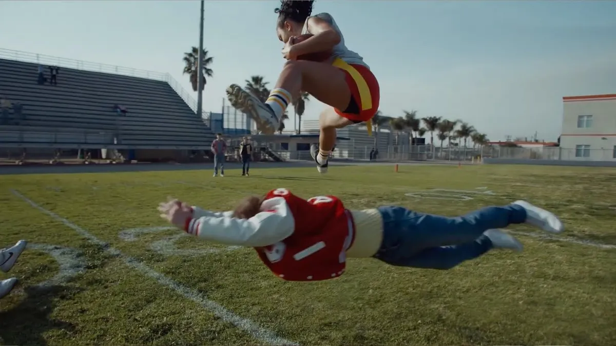 A female flag football player jumps over a male player in NFL's Flag 50 ad