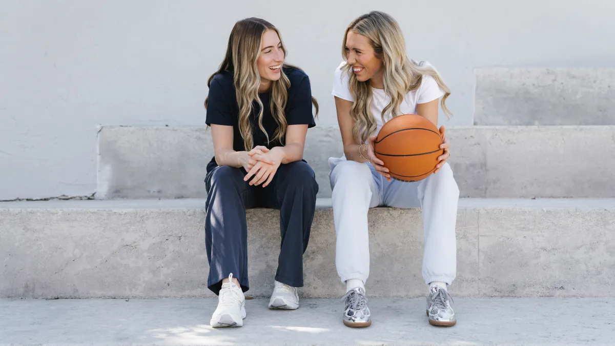 Lexie Hull and Kate Martin sit on a set of outdoor steps, holding a basketball and smiling.