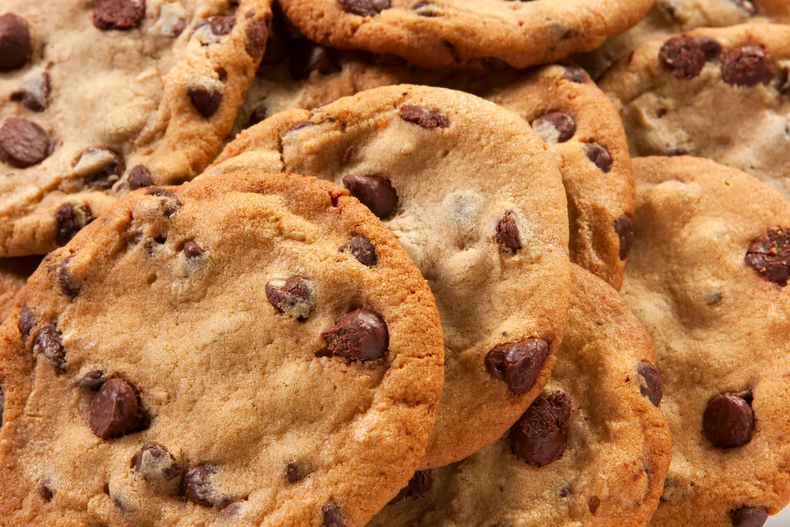 Piled up chocolate chip cookies fill the frame.