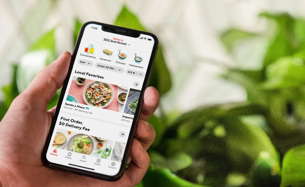 An image of a hand holding a smart phone with the DoorDash homepage.