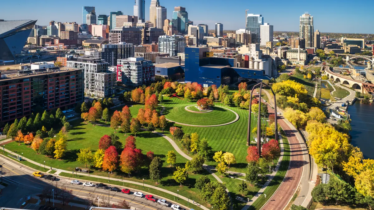 Trees with autumn color in field in front of tall buildings.