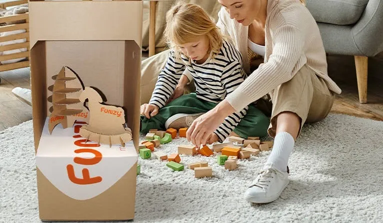 An adult and child play with toys and a cardboard box that has toy-shaped cutouts.