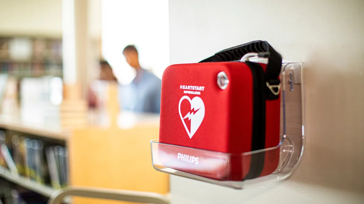 A red case with a picture of a heart and a lightning bolt and the word 'Philips' is on a plastic shelf fixed to a wall.