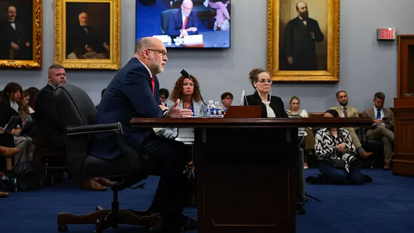 a sitting man surrounded by people testifies at a congressional hearing