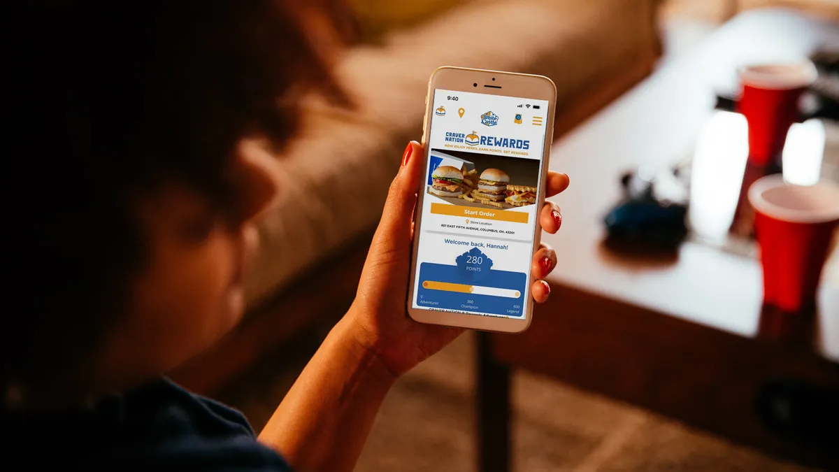 A woman holds a smartphone with the White Castle loyalty program prominently displayed