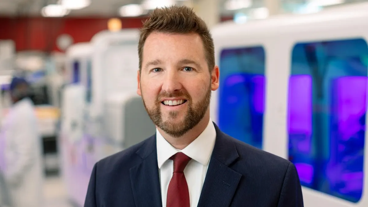 Portrait of Matthew Binnicker standing in front of lab equipment