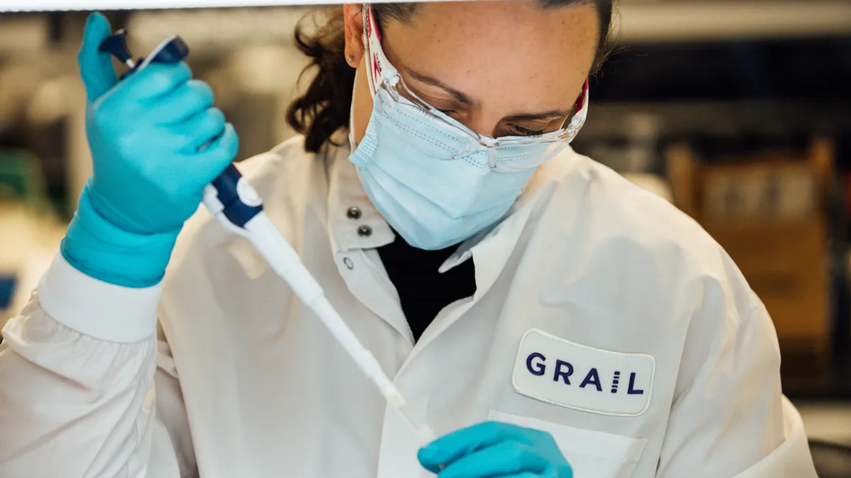 A person wearing safety goggles holds a pipette of fluid.