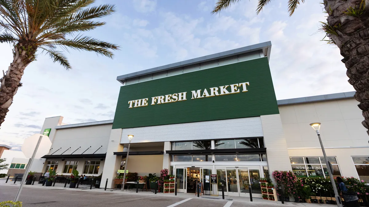 Exterior of The Fresh Market's Lakewood Ranch store with flowers out front, palm trees and a blue sky