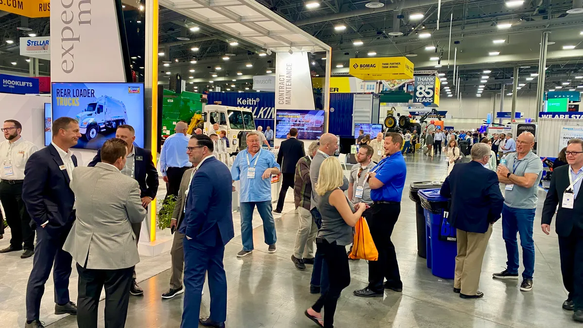 Several people walk in the exhibit hall of WasteExpo, surrounded by displays from companies