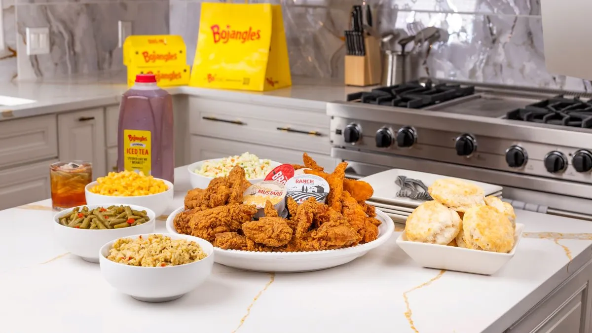 A phogrpah of fried chicken, biscuits and variuous sides on a white countertop with a yellow bag that says Bojangles in the background.