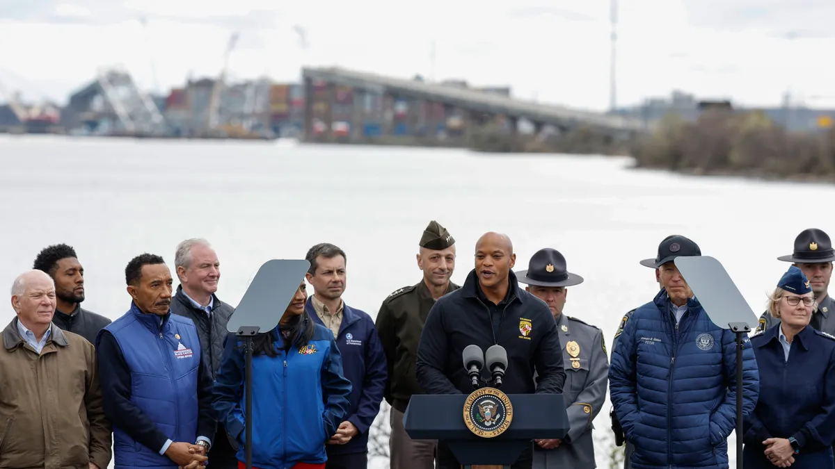 A group of people stand at around a speaker at a podium on the banks of a river.