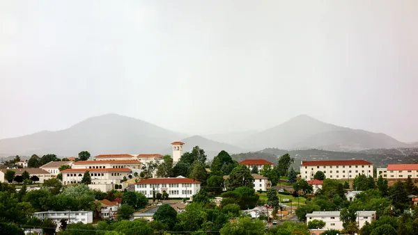 Campus with red tile roofs and white stucco buildings against backdrop of mountains.