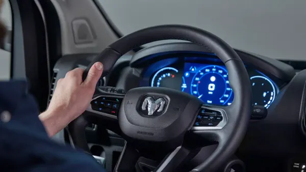 A driver behind the wheel of a 2026 Ram ProMaster van showing the steering wheel and instrument cluster.