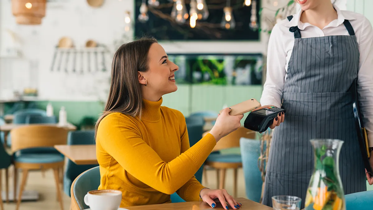 Woman paying contactless with mobile phone in cafe