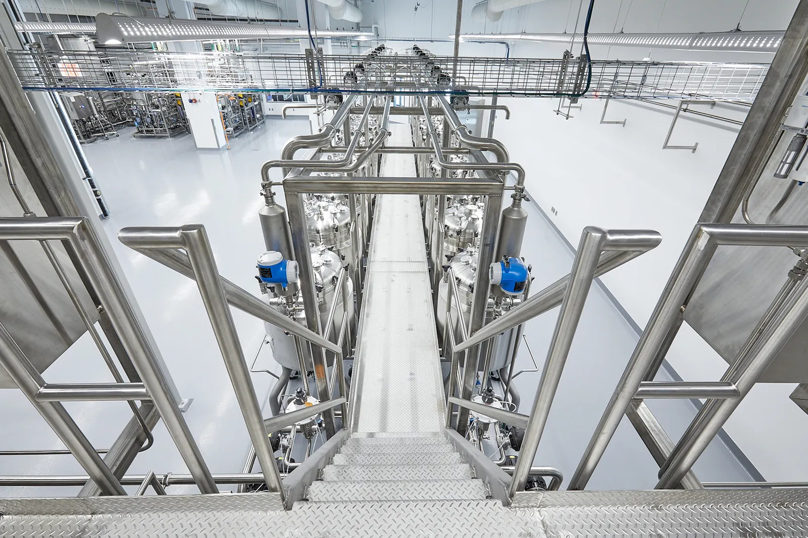A view from a silver catwalk of Upside Foods' bioreactors in its EPIC facility and the stairs and walkway for people to access the tops of the machines.