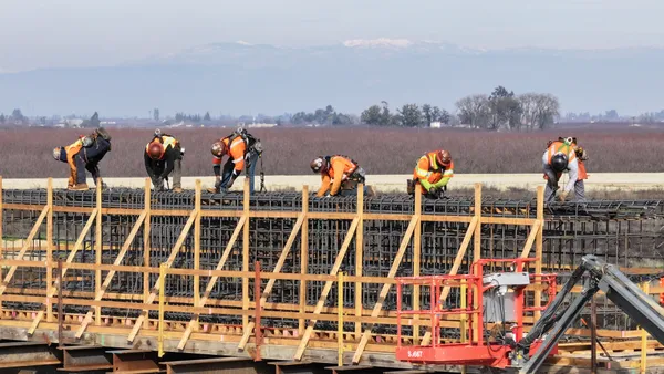 Six construction workers stand on rebar along a viaduct.