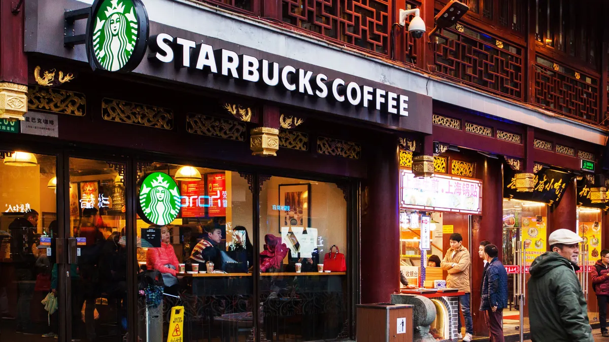 People sit inside a store drinking coffee. The sign of the store says Starbucks Coffee.
