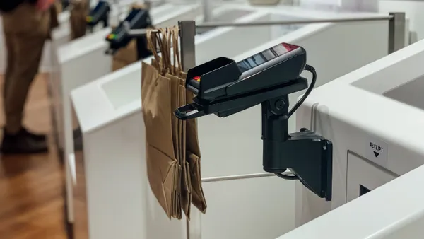 A close up of a payment terminal next to a white self checkout bin with paper bags hanging.