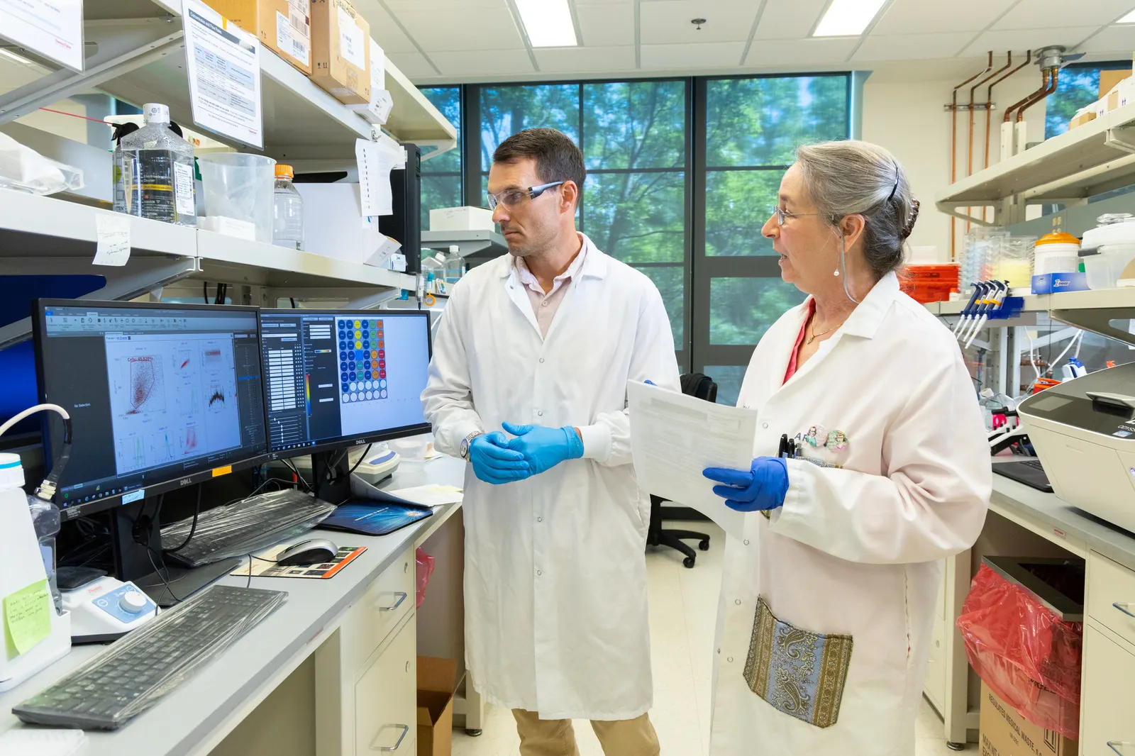 Two people in white coats stand next to a laboratory workbench