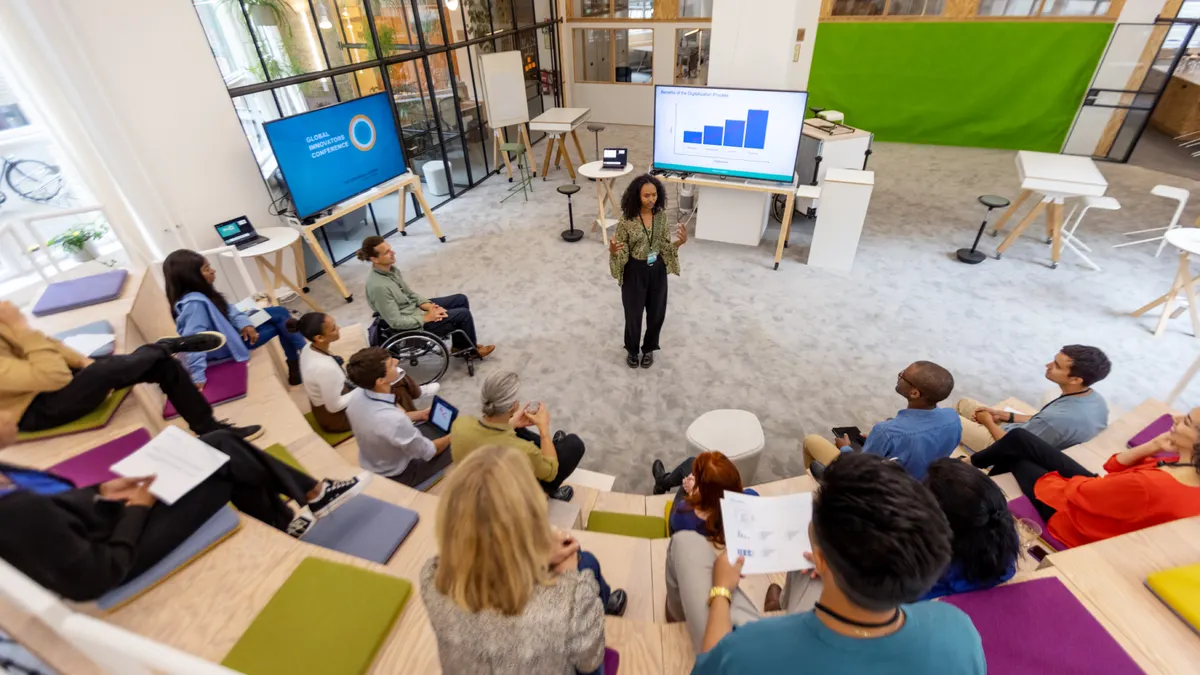 African woman giving speech to group of business people during startup launch event. Multiracial business professionals sitting at seminar hall and listening to young entrepreneur.