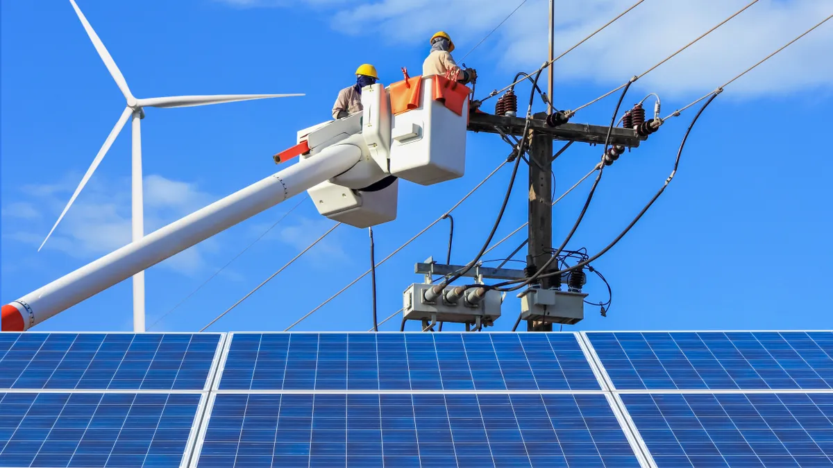 Electricians repairing wire of the power line on bucket hydraulic lifting platform vehicle with solar panels and wind turbines in power station