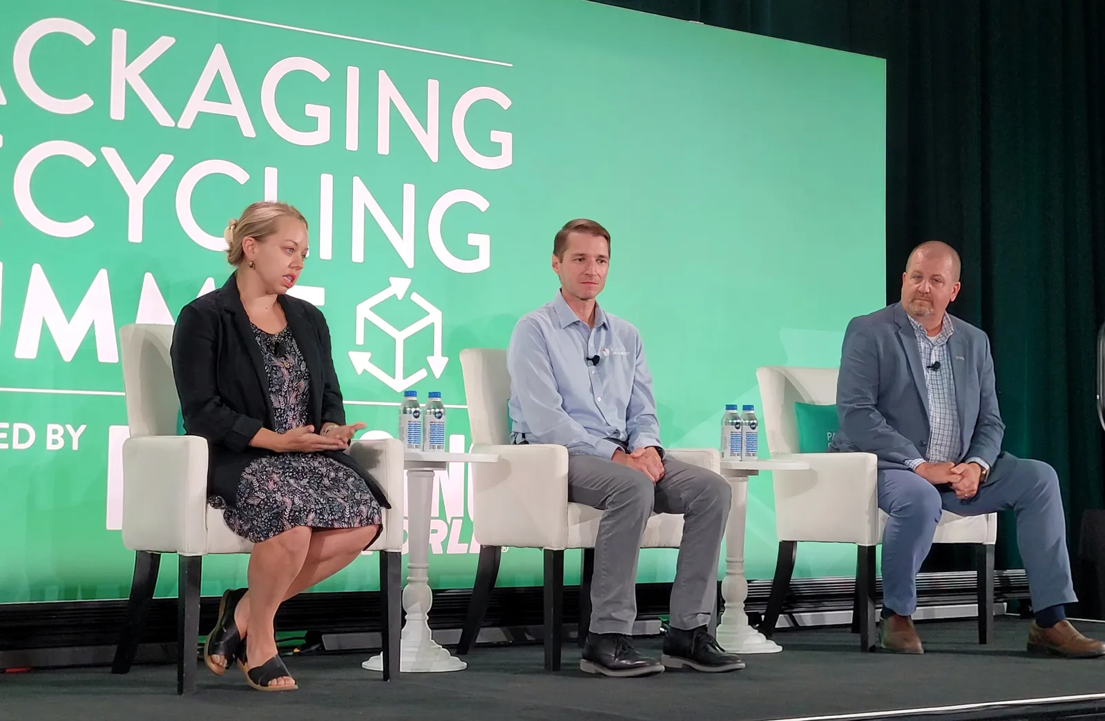 Three people sit on a stage during a panel discussion in front of a green background that says Packaging Recycling Summit.