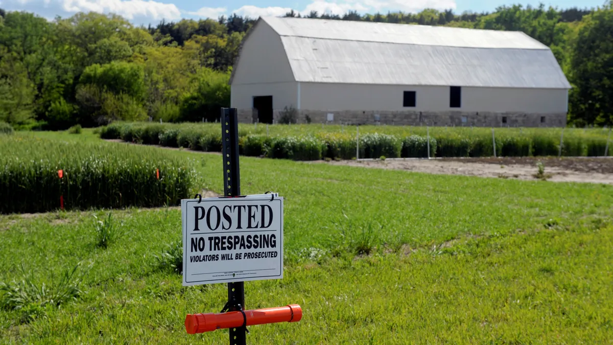 A barn is seen on a plot of farmland. In front, a sign reads "No trespassing"