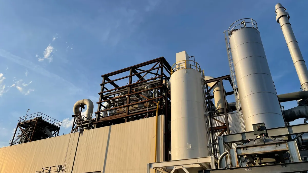 Exterior view looking up at the roof of an industrial facility with pipes, tanks and scaffolding.