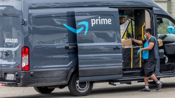 A worker wearing a mask and gloves stands outside of an Amazon Prime van containing packages.
