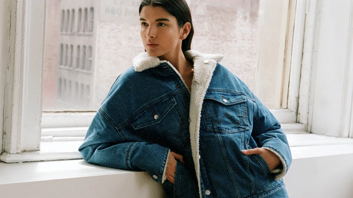 A person leans on a windowsill wearing a denim jacket lined in fuzzy material.