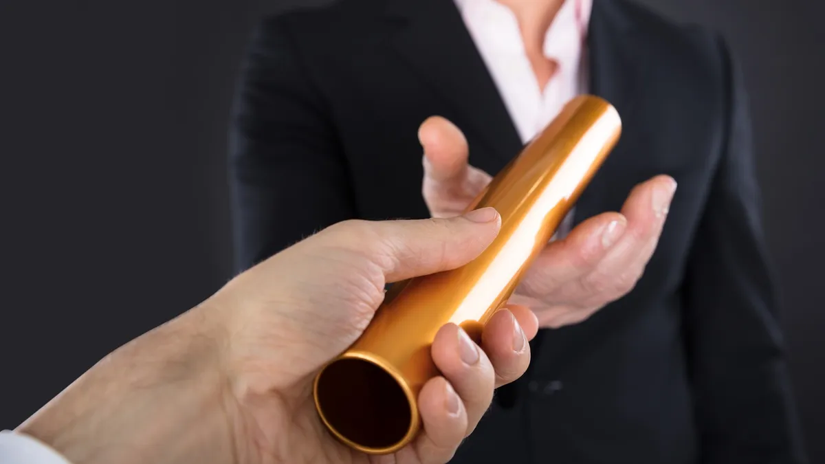 a Close-up photo Of A Businessperson Passing Golden Relay Baton To a Colleague.