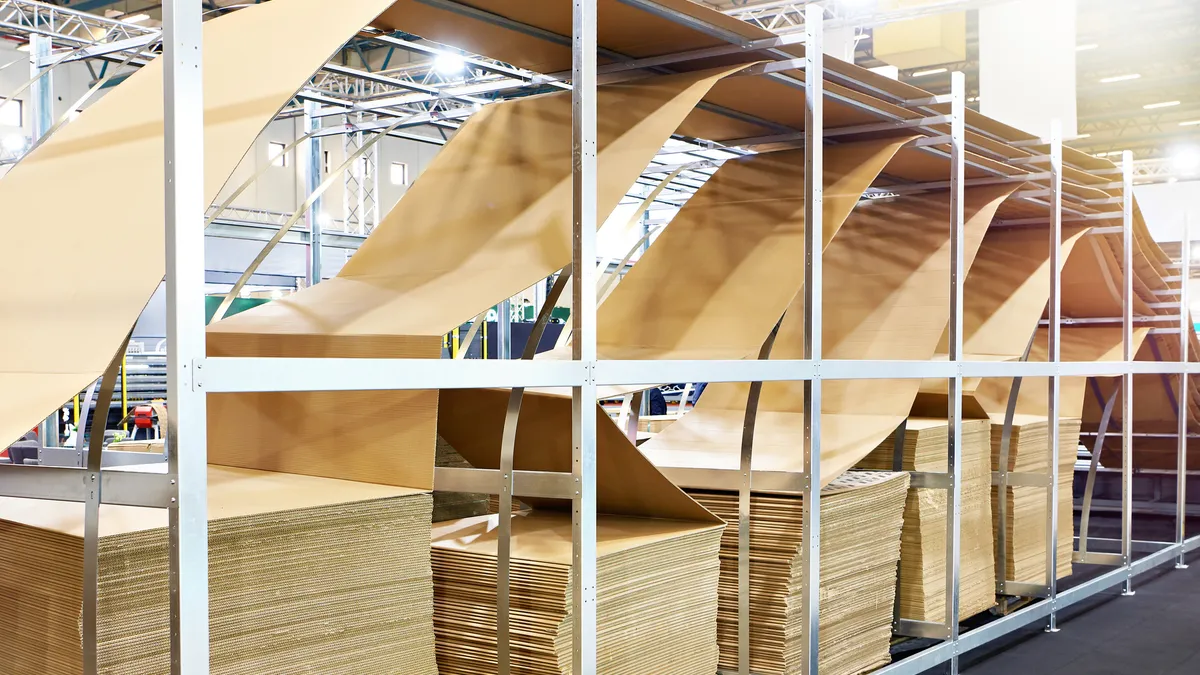 Sheets of cardboard get folded and stacked by industrial equipment on a manufacturing line.