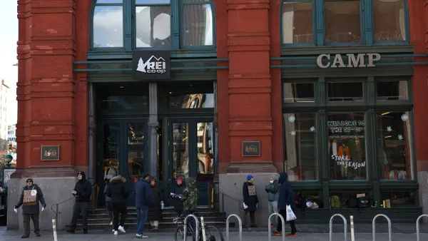 People stand outside a red brick REI store in New York City, with protest signs.