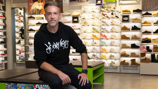A person sitting in a shoe store, wearing a hoodie.