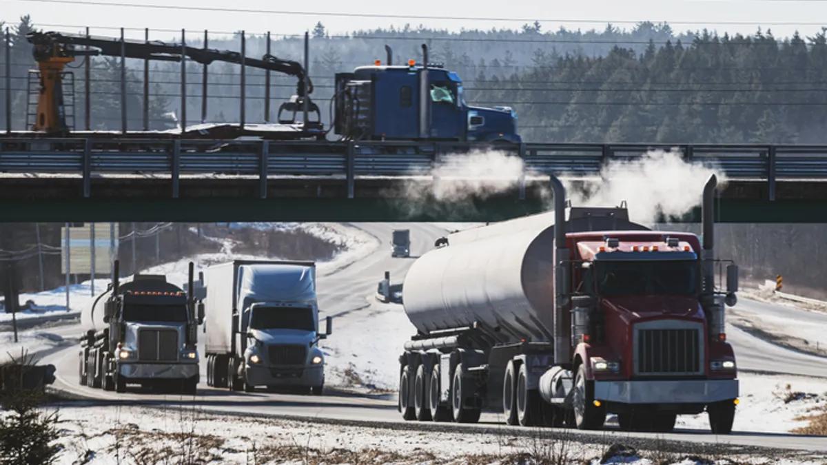 Trucks on the road and a bridge by snow-covered areas.