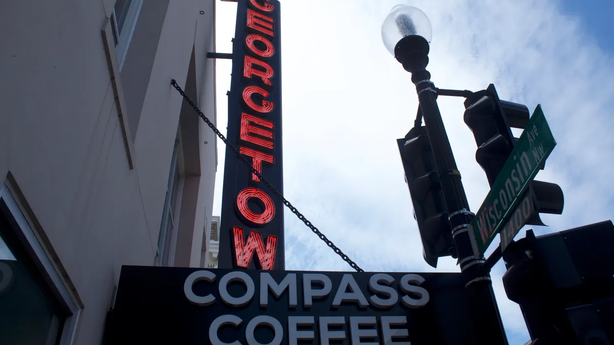 A white sign with black text reading 'Compass Coffee' in front of and below a lighted neon saying reading 'Georgetown'