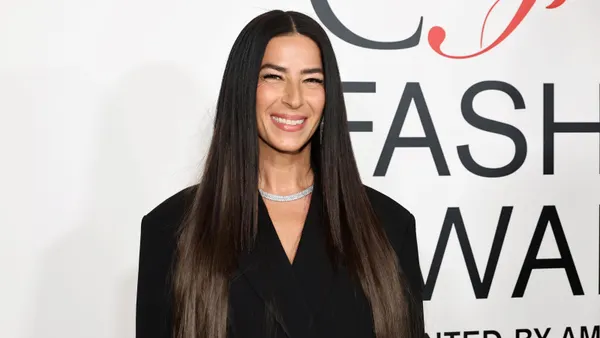 A person with long, straight, dark hair stands smiling at the camera in a close-up.