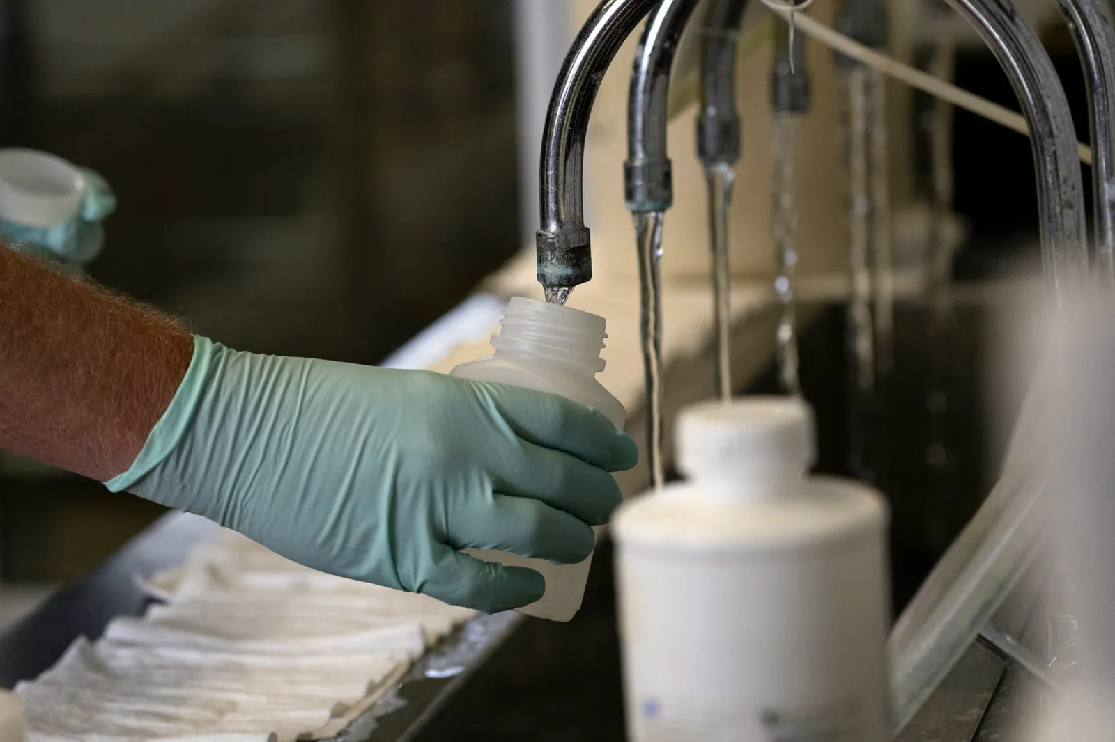 A hand holds a plastic container under a running faucet.