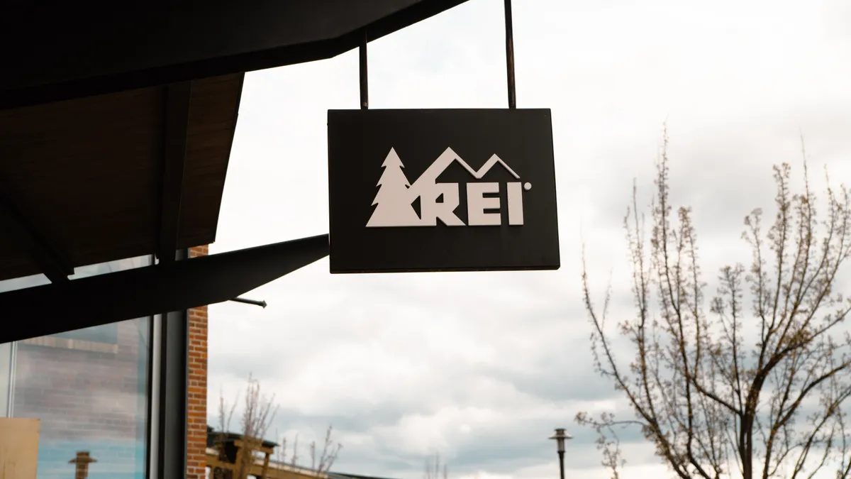 A hanging store sign with REI's logo on it.