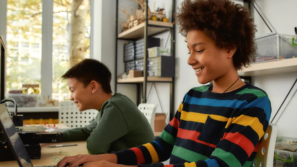 A student at a laptop in a classroom typing and smiling