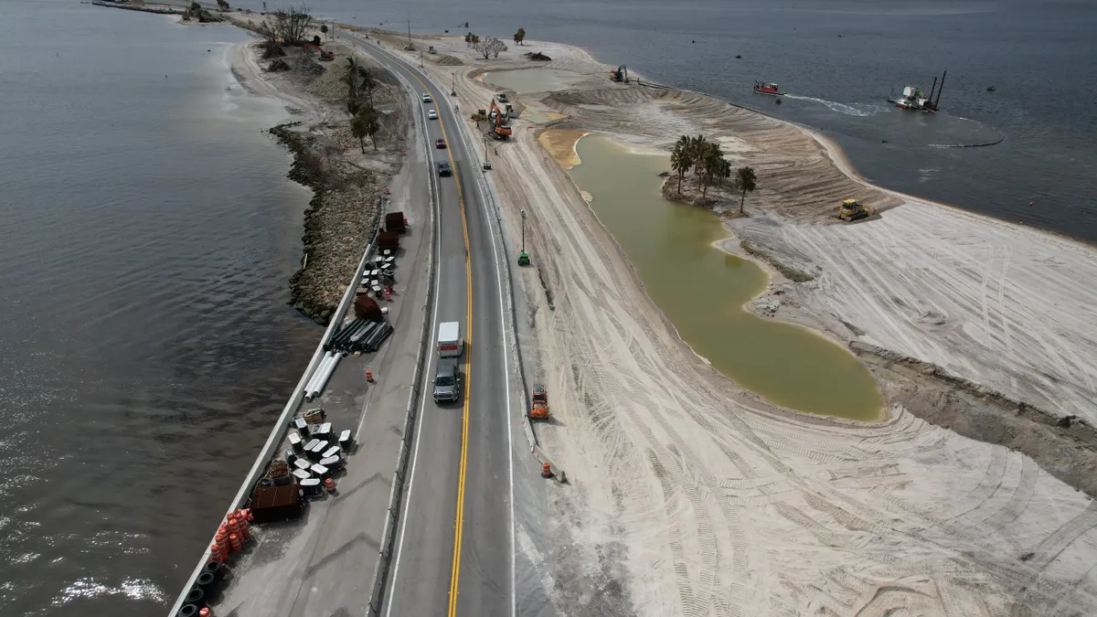 Aerial view of the long road that extends over water, with a few vehicles driving over it.